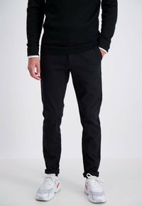 Zwarte broek met een slanke pasvorm, voorzien van zijzakken en een gladde textuur, gecombineerd met witte en grijze sneakers.