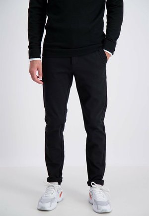 Zwarte broeken van gladde stof, met een slim fit, zijzakken en subtiele stiksels, gedragen met witte sneakers.