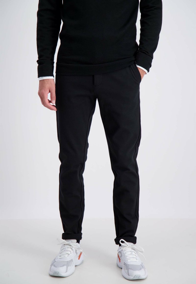 Zwarte broek met een slanke pasvorm, voorzien van zijzakken en een gladde textuur, gecombineerd met witte en grijze sneakers.