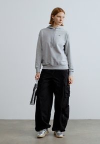 Hall hall puuvillane kapuutsiga pusa paeladega, mis on kombineeritud laia lõikega mustade taskutega cargo-pükstega. Hõbedased tossud ja metallik värvi kott.