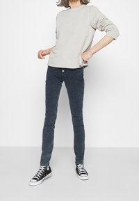 Sudadera gris claro con cuello redondo y puños equipados, combinada con jeans ajustados azul oscuro y zapatillas altas negras.