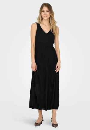 Abito maxi plissettato nero con scollo a V, dotato di una parte superiore aderente e una gonna fluida. Abbinato a delle scarpe con tacco a slingback con stampa leopardata.