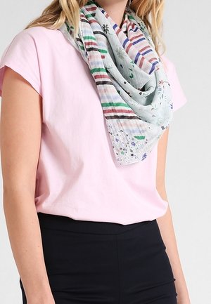 Femme portant une chemise à manches courtes rose clair et une écharpe multicolore à rayures et motifs floraux drapée autour du cou.