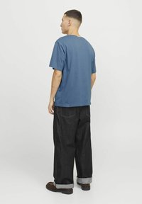 Blaues Baumwoll-T-Shirt mit kurzen Ärmeln, kombiniert mit schwarzen weit geschnittenen Jeans mit umgeschlagenen Säumen und sichtbaren Nähten.