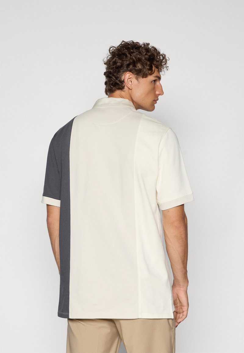 Polo de manga corta con un diseño de bloques de color que presenta paneles en crema y gris oscuro, fabricado en una suave mezcla de algodón.