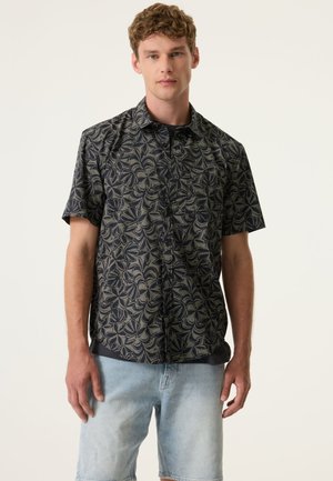 Korte mouw blouse van donker stof met een bladprint in goud. Voorzien van een button-down kraag en een ontspannen pasvorm. Draagt samen met lichte denim shorts.