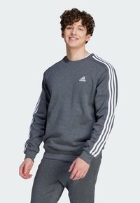 Felpa grigia realizzata in tessuto morbido, con logo Adidas bianco sul petto e tre strisce bianche lungo le maniche.