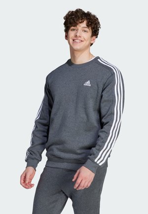 Sweatshirt gris en tissu doux, avec un logo Adidas blanc sur la poitrine et trois bandes blanches le long des manches.