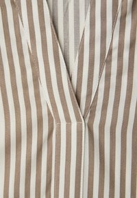 Tissu à rayures verticales beige et blanc avec des coutures formant un col en V sur un vêtement.