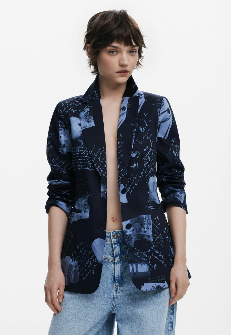 Blazer marine avec un collage d'imprimés graphiques bleus et de texte manuscrit, avec des manches retroussées et une coupe ajustée.