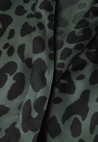 Leopardmönstrat tyg i mörkgrön och svart, med en slät yta som har oregelbundet formade fläckar och kontrasterande sydda sömmar.