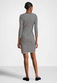 Stripet kjole med lange ermer, med svarte og kremfargede horisontale striper. Slank passform med rygglomme og knelengde snitt.