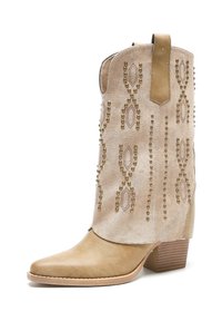 Botas de vaquero de ante beige con patrones decorativos de cuentas, punta afilada y tacón apilado. Presenta un tirador para facilitar su uso.