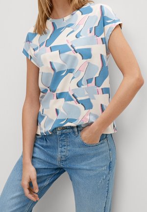 Personne portant une chemise à manches courtes à motifs abstraits bleus, roses et blancs, rentrée dans un pantalon en jean taille haute bleu clair.