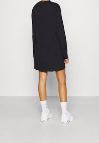 Svart långärmad klänning med rak passform, mjukt material och rundad halsringning. Kombinerad med vita sneakers och strumpor.