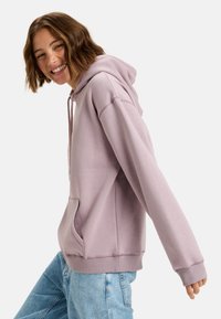 Ljuslila hoodie i mjukt material, med en framficka och ribbade ärmslut, kombinerad med ljusblå denimjeans.