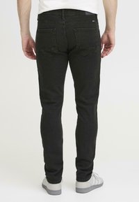 Blugi din denim negri, cu o croială slim, care au două buzunare pe spate, cusături subtile și un talie medie. Purtați cu adidași gri.