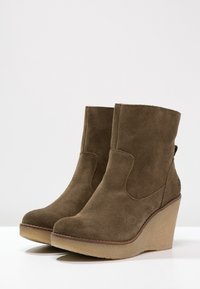 Stivaletti alla caviglia in suede marrone con tacco a zeppa, caratterizzati da una texture liscia e un design elegante e minimalista. Nessuna ferramenta o decorazione visibile.