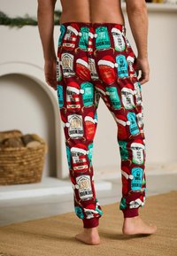 Red pajama pants featuring a colorful, festive print of beer labels and Santa hats, with an elastic waistband and ribbed cuffs.