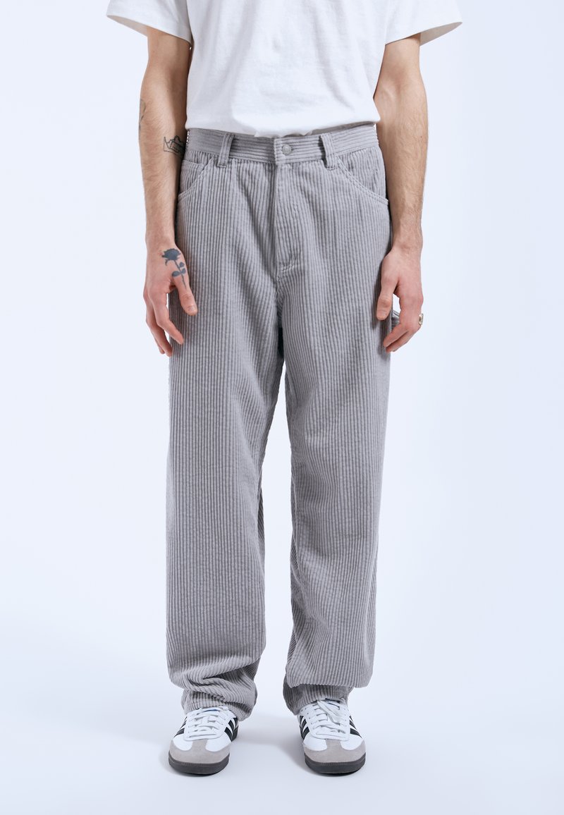 Grijze corduroy broek met een verticale streepprint, voorzien van een knoopsluiting, zijzakken en een ontspannen pasvorm. Draagt met witte sneakers.