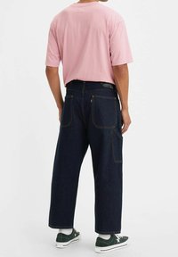 Ljusrosa t-shirt med kort ärm i kombination med mörkblå vida denimjeans som har två bakfickor och kontrasterande sömdetaljer.