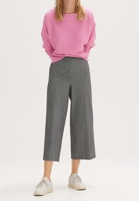 Pull rose côtelé à coupe décontractée, associé à un pantalon large à carreaux gris. Chaussures blanches.