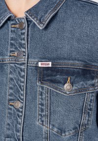 Kurtka jeansowa w jasnoniebieskim kolorze z klasycznym kołnierzem, dwoma kieszeniami na piersi, metalowymi guzikami oraz tkowaną metką z logo na lewej kieszeni.