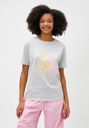 Szary bawełniany t-shirt z grafiką słońca i symbolu yin-yang w kolorze żółtym i różowym, z napisem "ZNAJDŹ SWOJĄ RÓWNOWAGĘ" wydrukowanym poniżej.