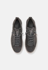 Sive suede tenisice s elastičnim vezicama, teksturiranim gornjim dijelom i ravnim gumenim potplatima. Unutrašnjost ima oznaku "SUPER SOFT" i uzorak na postavu.