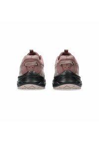 Un par de zapatillas deportivas de color rosa polvo con suelas intermedias negras, vistas desde atrás, mostrando los lazos en el talón y las suelas texturizadas sobre un fondo blanco.