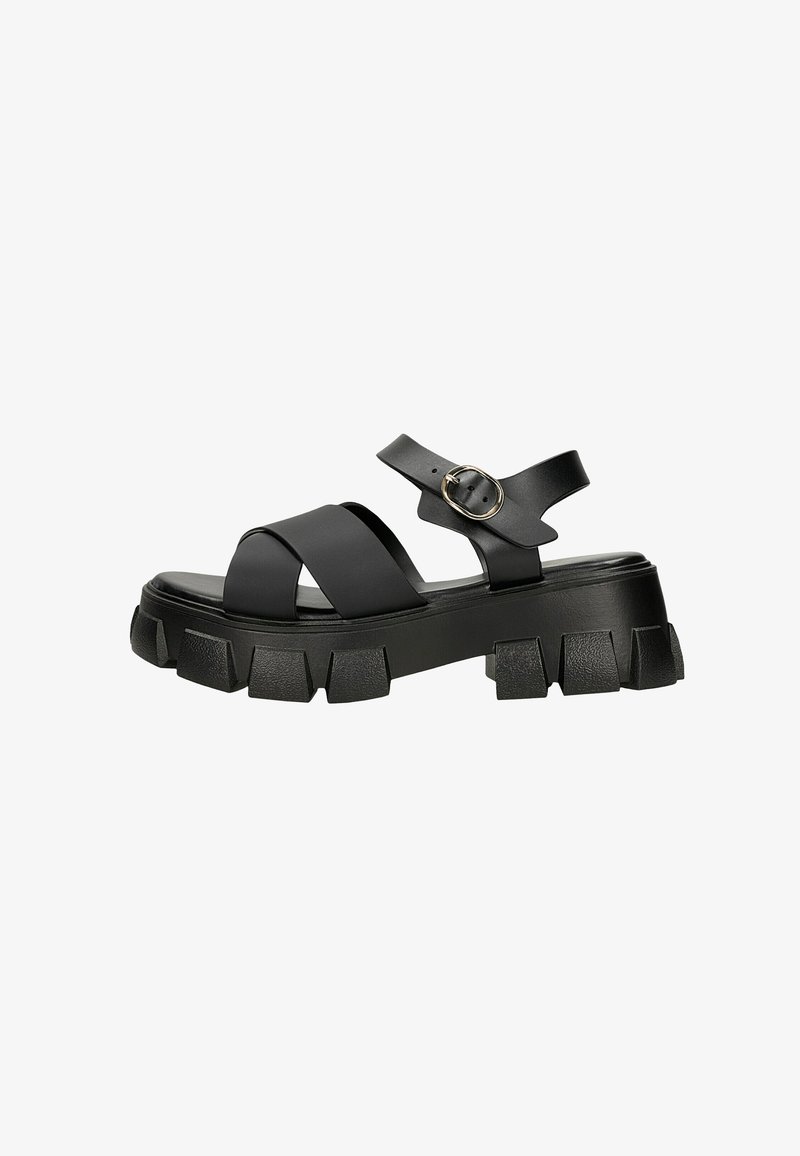 Μαύρο chunky πλατφόρμα σανδάλι με χοντρές διασταυρωμένες λουρίδες και λουράκι αστραγάλου που στερεώνεται με στρογγυλό χρυσό αγκράφα.