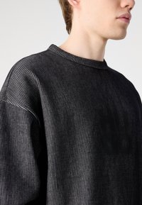 Sorte stripete hettegenser med ribbet rund hals og teksturert stoff. Har senkede skuldre og en avslappet passform. Minimale design detaljer.