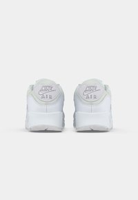 White Nike Air sneakers with textured mint-green accents at the heel, featuring embossed branding. Rounded shape with a thick white sole.