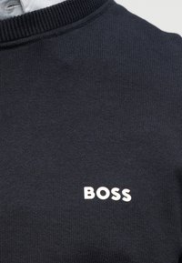Μπλε ναυτικό πουλόβερ με υφασμένο ανάγλυφο σχέδιο και ριμπ γιακά, με λευκό λογότυπο "BOSS" στο μπροστινό μέρος.