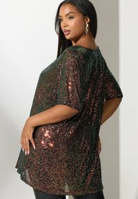 Top con lentejuelas de corte holgado que presenta lentejuelas multicolores sobre una tela oscura, con mangas cortas y un cuello redondo.