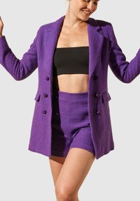 Blazer violet texturé avec short assorti. Le blazer présente un col cranté et deux boutons ; le short a une coupe ajustée et une ceinture lisse.