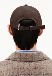 Braune Baseballmütze aus strapazierfähigem Material, mit einem hinteren Riemen und einer Metallschnalle sowie einem Etikett an der Seite.