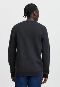 Maglione lavorato a maglia grigio scuro con una finitura texturizzata, scollatura tonda e polsini a costine. Presenta un colore uniforme e un dettaglio nella vita inferiore.