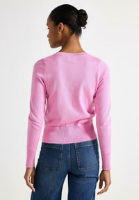 Vaaleanpunainen neulepaita, jossa on pyöreä kaula-aukko sekä resorit hihoissa ja helmassa. Yhdistetty tummansinisisiin farkkuihin.