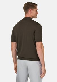 Ciemnozielona koszulka polo z krótkim rękawem o prążkowanej fakturze i kołnierzyku. Ubrana ze spodenkami o jasnym kolorze, z prostym obrzeżem.