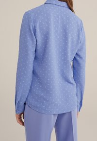 Ljusblå skjorta med ett strukturerat mönster, långa ärmar och krage. Har knappmanschetter och en lätt formning bak.