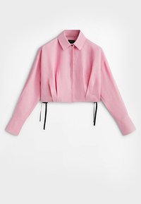 Chemise rose recadrée à manches longues avec col pointu, patte de boutonnage cachée, cordons latéraux noirs réglables et larges poignets.