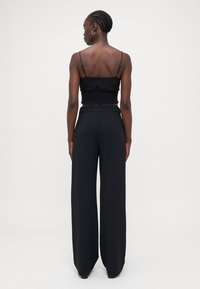 Black crop top with textured knit design and spaghetti straps, paired with high-waisted wide-leg black trousers.