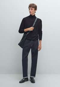 Svart polotröja, mörka denimbyxor med uppvikta fållar, svarta läderskor och en svart axelväska. Släta texturer, minimalistisk design.