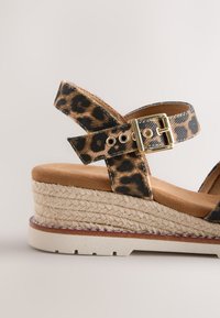 Sandale compensée avec brides imprimé léopard, boucle dorée, plateforme en jute tressée et semelle blanche texturée.