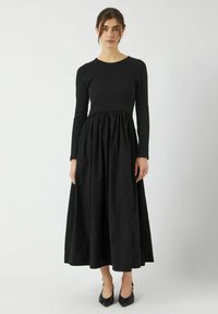 Abito lungo nero con maniche lunghe, un corpetto aderente e una gonna ampia e arricciata. Realizzato in tessuto leggero con una superficie liscia.