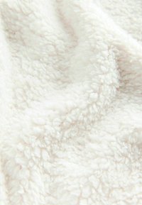 Couverture blanche et moelleuse avec une surface douce et texturée. Le tissu présente un motif en relief, créant une apparence confortable.