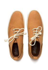 Des chaussures en cuir marron avec des lacets blancs et un bout arrondi, présentant des coutures le long des bords et une surface texturée.
