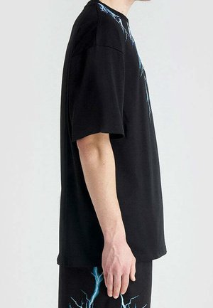 Camiseta negra de manga corta con un patrón de relámpagos en azul a lo largo de los hombros, hecha de algodón suave, con un corte holgado.