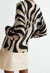 Maglione beige con strisce nere a zebra, maniche lunghe, polsini a costine e una trama scintillante. Abbinato a una gonna di pelle chiara.